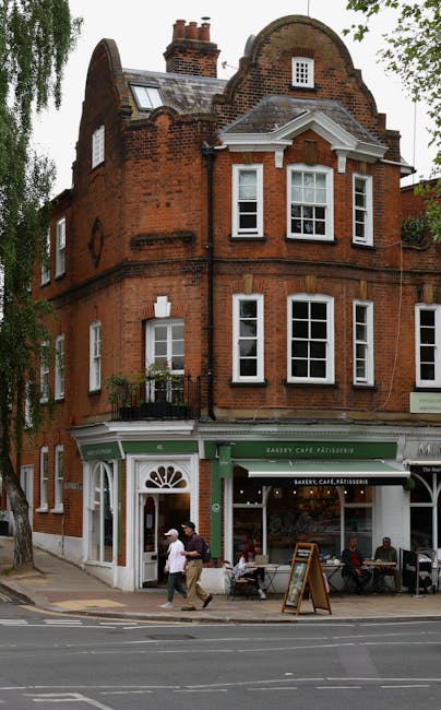 Street-level view of a historic red brick building with large white-framed sash windows, housing a bakery, café, and patisserie on the ground floor. The storefront features a green awning with signage